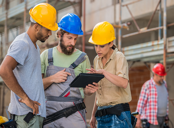 Two men and a women at a construction site looking a digital tablet