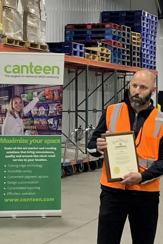 Canteen employee receiving award whle standing in warehouse
