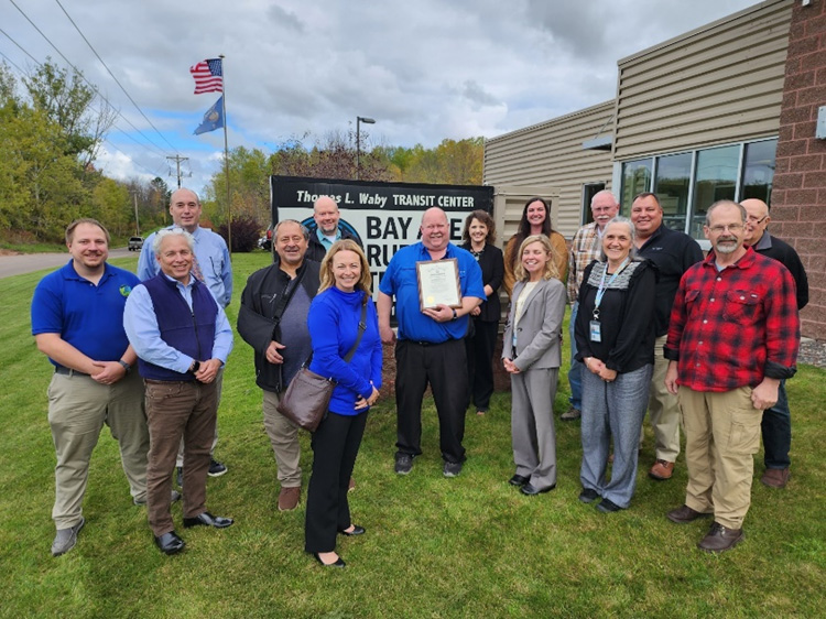 Bay Area Rural Transit Manager Pat Daoust, center, holds an Exemplary Employer award surrounded by area leaders in front of the Ashland organization's sign. 