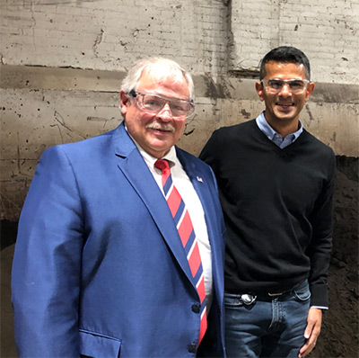 Outgoing Chair of the Governor's Council on Workforce Investment S. Mark Tyler, left, and new Chair Sachin Shivaram recently toured Wisconsin Aluminum Foundry growing operations in Manitowoc, where Shivaram serves as CEO. Behind them is 'green' sand, which is reused multiple times in the aluminum casting process as part of the foundry's commitment to environmental sustainability. 
